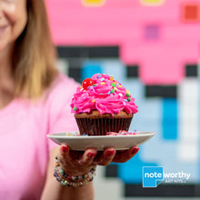 Load image into Gallery viewer, woman holding pink cupcake in front of post-it note pixel art mural