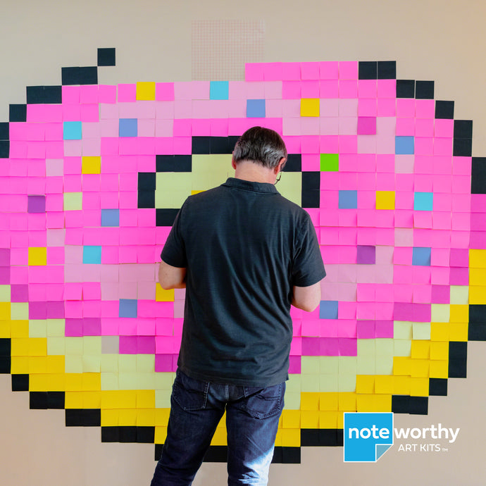 Man making post it note mural of giant pixel art donut