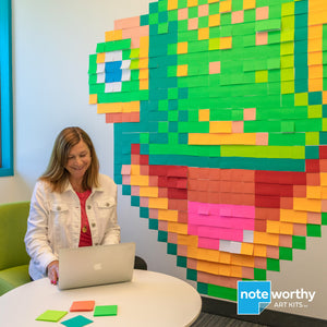 Woman sitting in front of large post it note wall mural of pixel art gecko